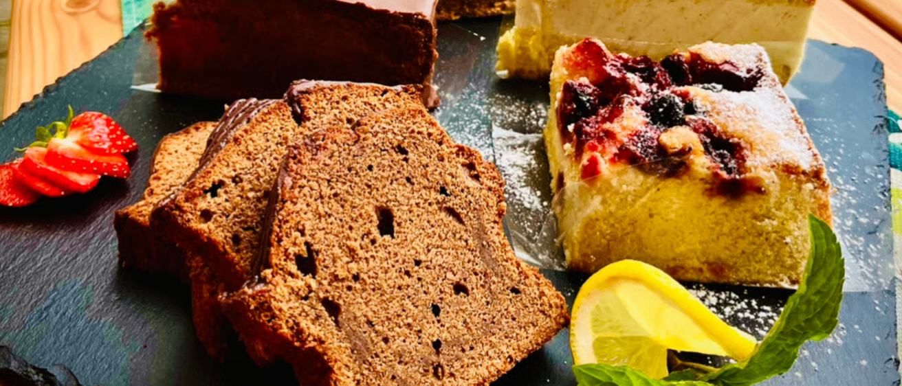 Eine Auswahl an Desserts auf einem Holztisch, darunter Schokoladenkuchen, fruchtbedeckter Kuchen und Zitronenscheiben mit Minzblättern.