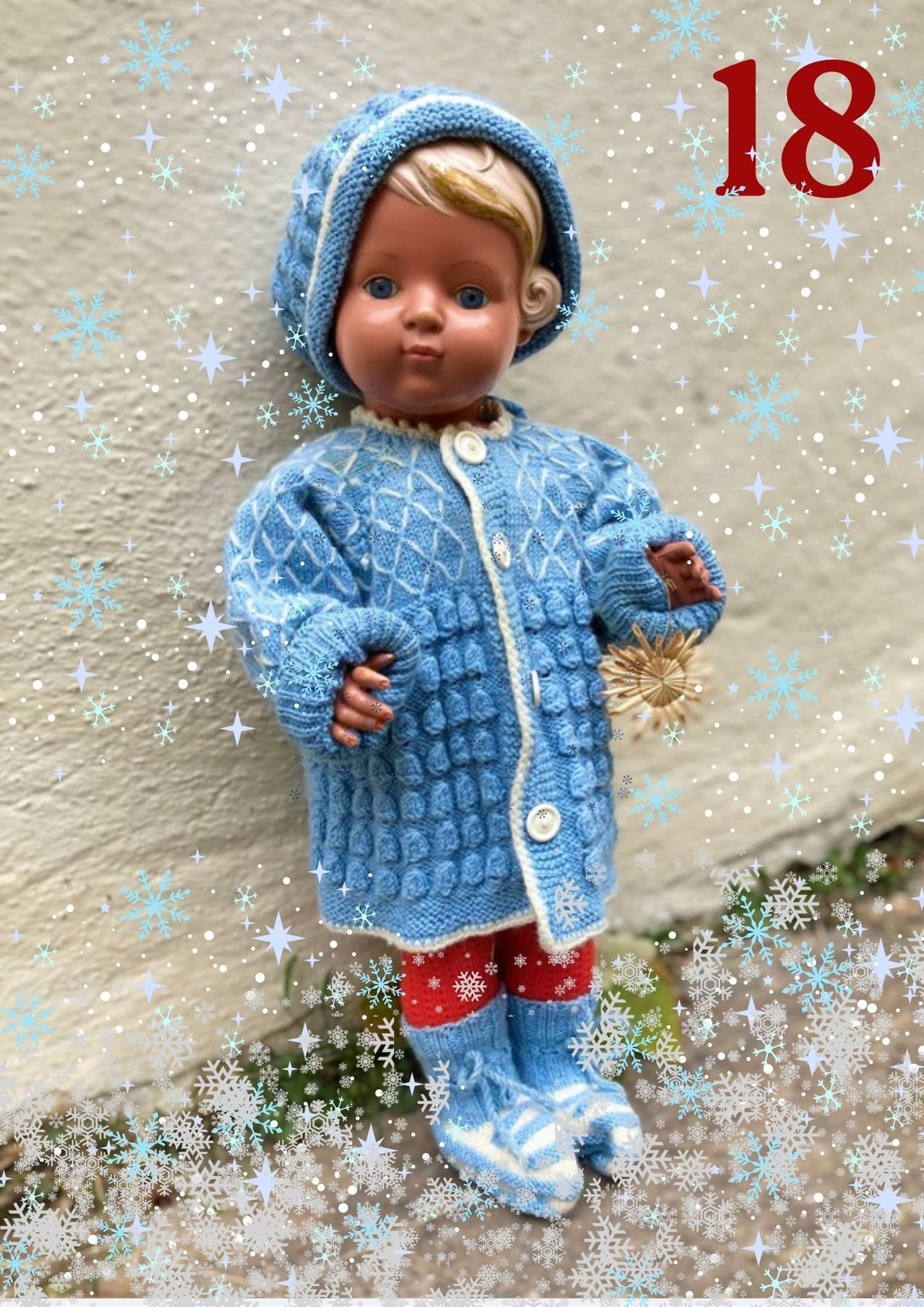 Eine Puppe, gekleidet in einem hellblauen gestrickten Mantel, roten Hosen und blauen Stiefeln, steht vor einem weißen Hintergrund mit Schneeflocken.