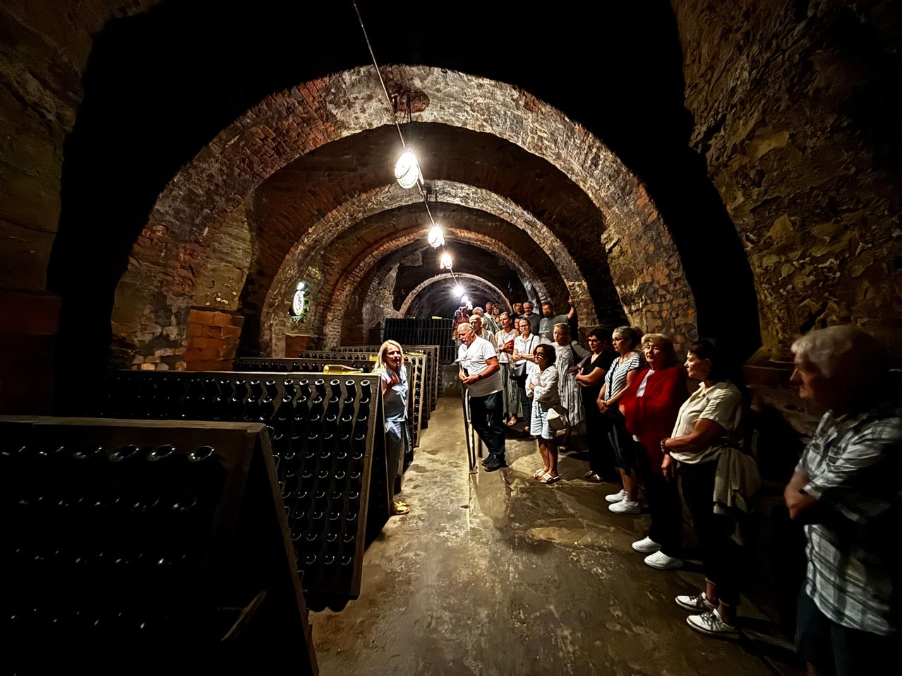 Besucher in einem Keller mit vielen Flaschen und Ziegelbögen