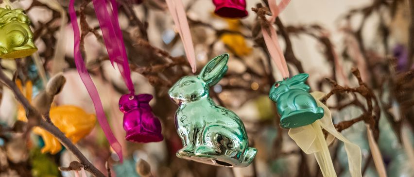 A branch with colorful Easter decorations, including metallic bunnies and an Easter duck, all adorned with ribbons. The bunnies are green, pink, and yellow, while the duck is teal.