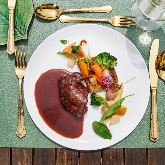 Ein weißer Teller mit Steak, roter Sauce und einer Vielzahl von Gemüse. Ein Weinglas und Besteck sind auf dem Tisch.