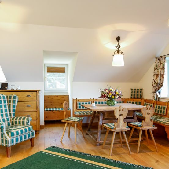 Ein Dachzimmer mit Holzmöbeln, einem Esstisch mit Blumen und einem Fenster mit Vorhängen.