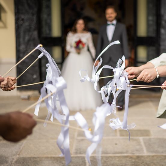 Eine Hochzeitszeremonie mit der Braut und dem Bräutigam, die sich an den Händen halten, mit weißen Bändern, die von anderen gehalten werden.