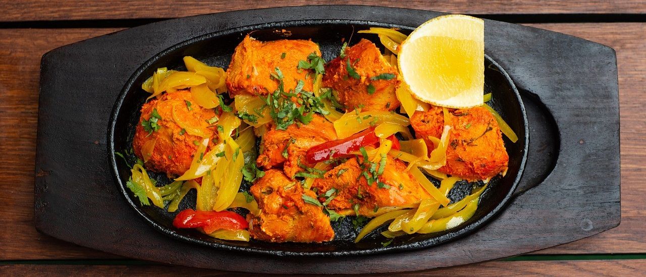 Ein Teller mit Chicken Tikka Masala mit Paprika und Zitrone auf einem Holztisch