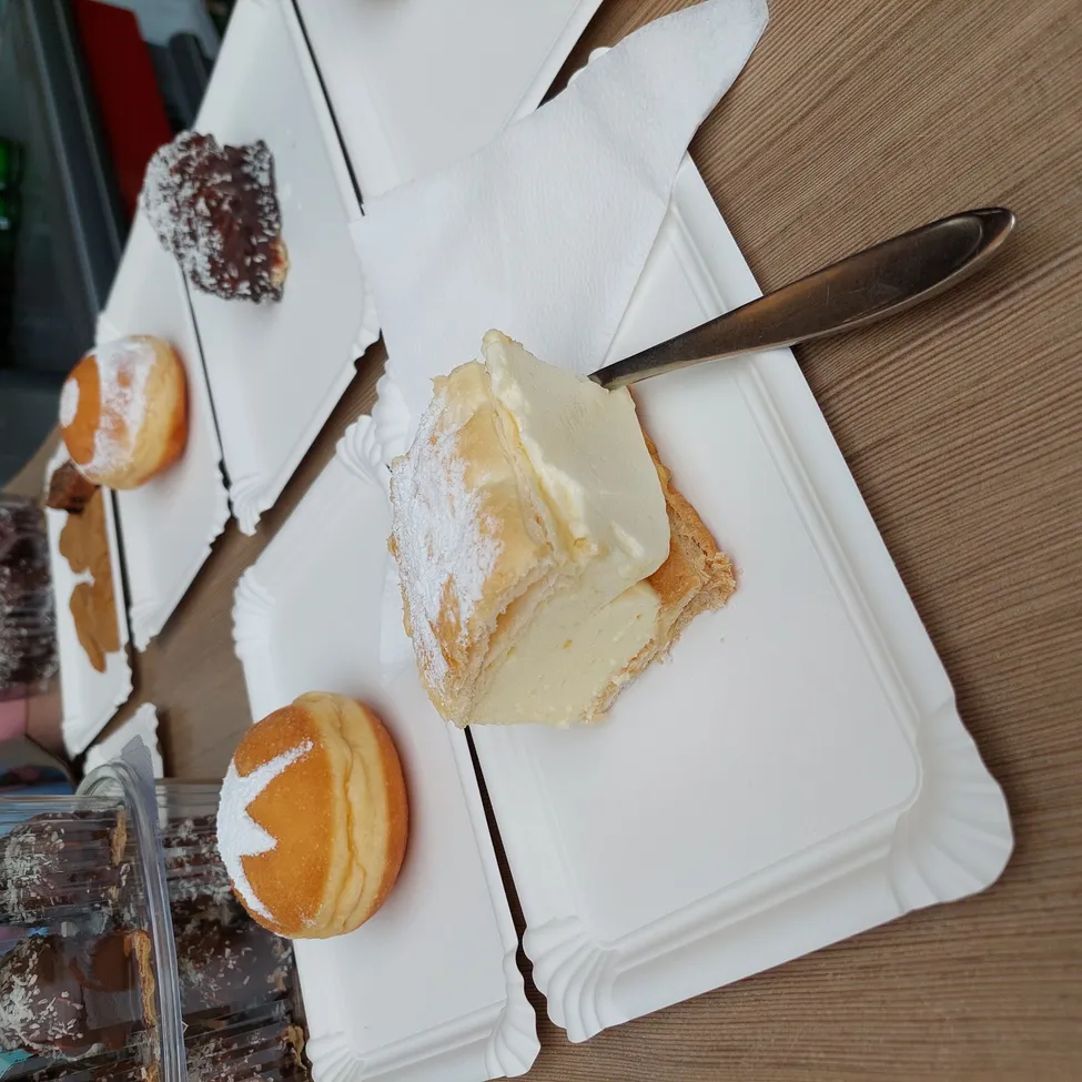 Einige Desserts sind auf weißen Tellern auf einem Holztisch serviert. Ein Gebäck ist mit Schlagsahne und einem silbernen Messer bestrichen.