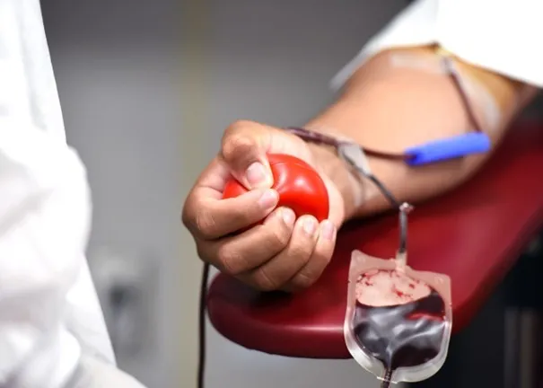 Eine Person drückt einen roten Ball, während sie Blut in eine Blutbeutel spendet, der mit ihrem Arm verbunden ist.