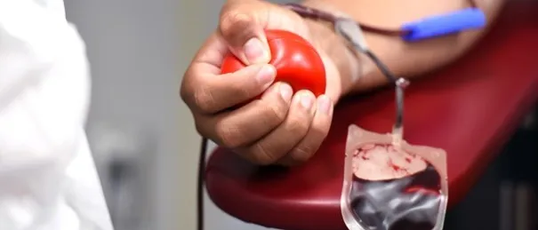 Eine Person spendet Blut in einer medizinischen Einrichtung. Die Person drückt einen roten Ball, während ein Blutbeutel an ihrem Arm angeschlossen ist.