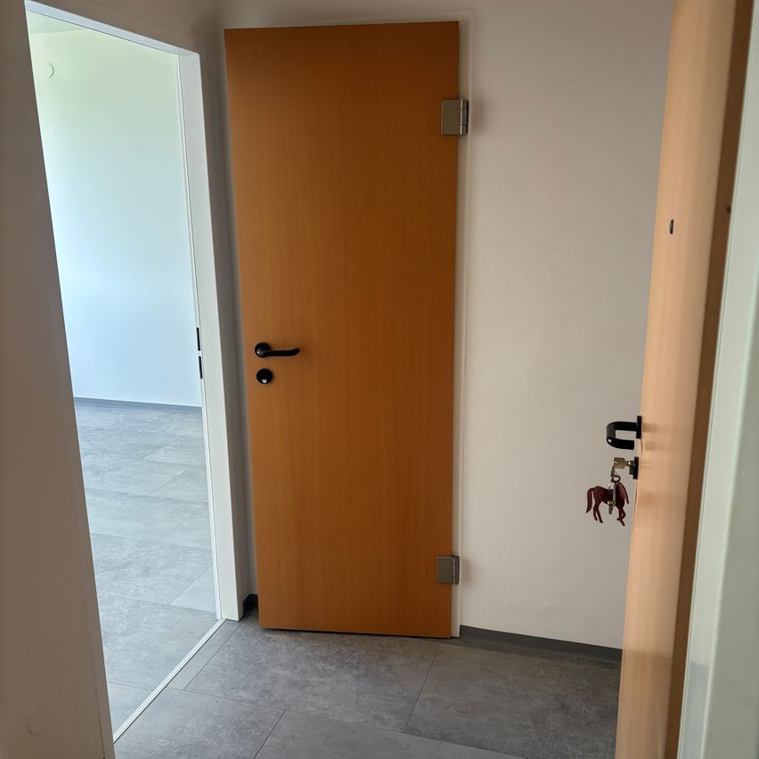 Ein leerer Raum mit einer geschlossenen Holztür und einem glänzenden Schlüssel mit Pferdedesign an der Wand.