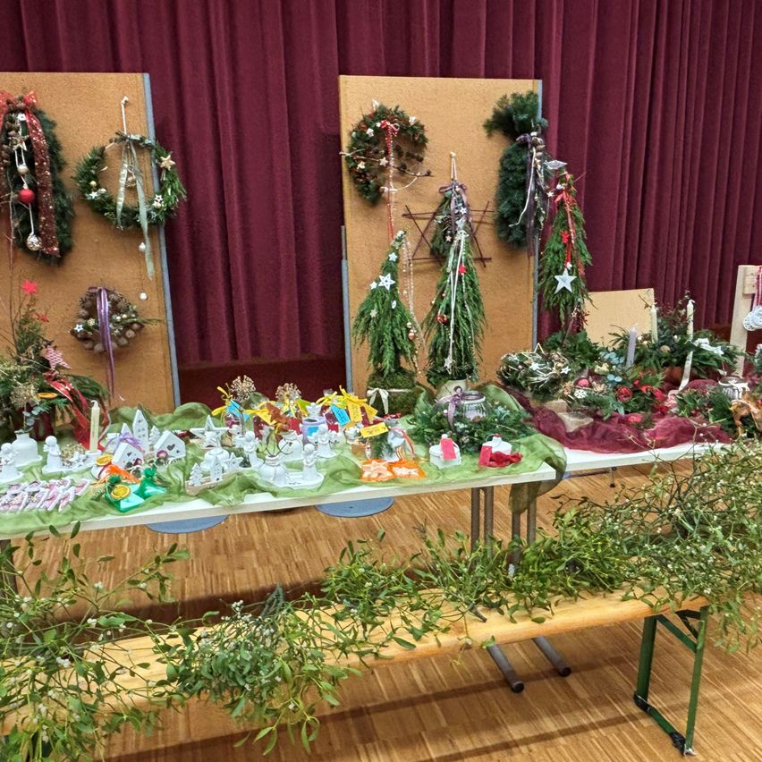 Eine festliche Ausstellung verschiedener Weihnachtsdekorationen, einschließlich Kränze, Sterne und andere Ornamente, ist auf einem Tisch in einem Raum mit Holzboden aufgebaut.