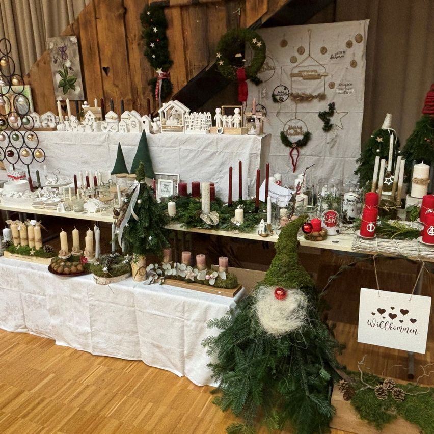 Eine festliche Ausstellung von Weihnachtsdekorationen, einschließlich Gnomfiguren, Kerzen, Kränzen und Ornamenten. Die Szene ist in einem Raum mit Holzböden und Wänden eingerichtet.