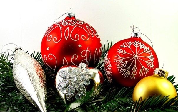 Eine Sammlung von Weihnachtskugeln, darunter rote, goldene und silberne, ruht auf Tannenzweigen. Die Ornamente variieren in ihrem Design, von Blumen- bis Schneeflockenmustern.