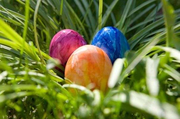 Drei bunte Ostereier liegen in einem Grasbereich. Die Eier sind in verschiedenen Farben, darunter pink, blau und orange.