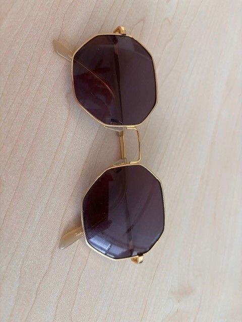 Ein Paar goldfarbener Sonnenbrille mit dunklen Gläsern auf einer Holzoberfläche.
