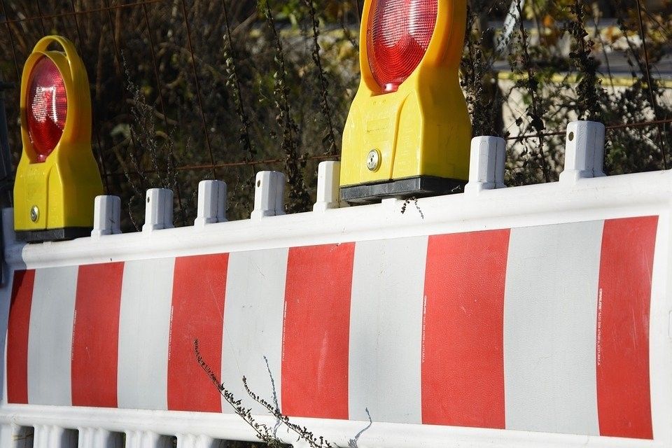 A red and white striped barrier with a yellow light on top is in front of a fence.