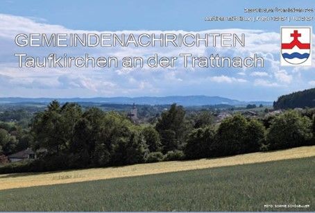 Eine Landschaft mit einem Feld und Bäumen, mit einem Logo und einem Titel oben. Der Titel lautet 'Gemeindenachrichten Taufkirchen an der Trattnach.' Der Himmel ist blau mit Wolken.