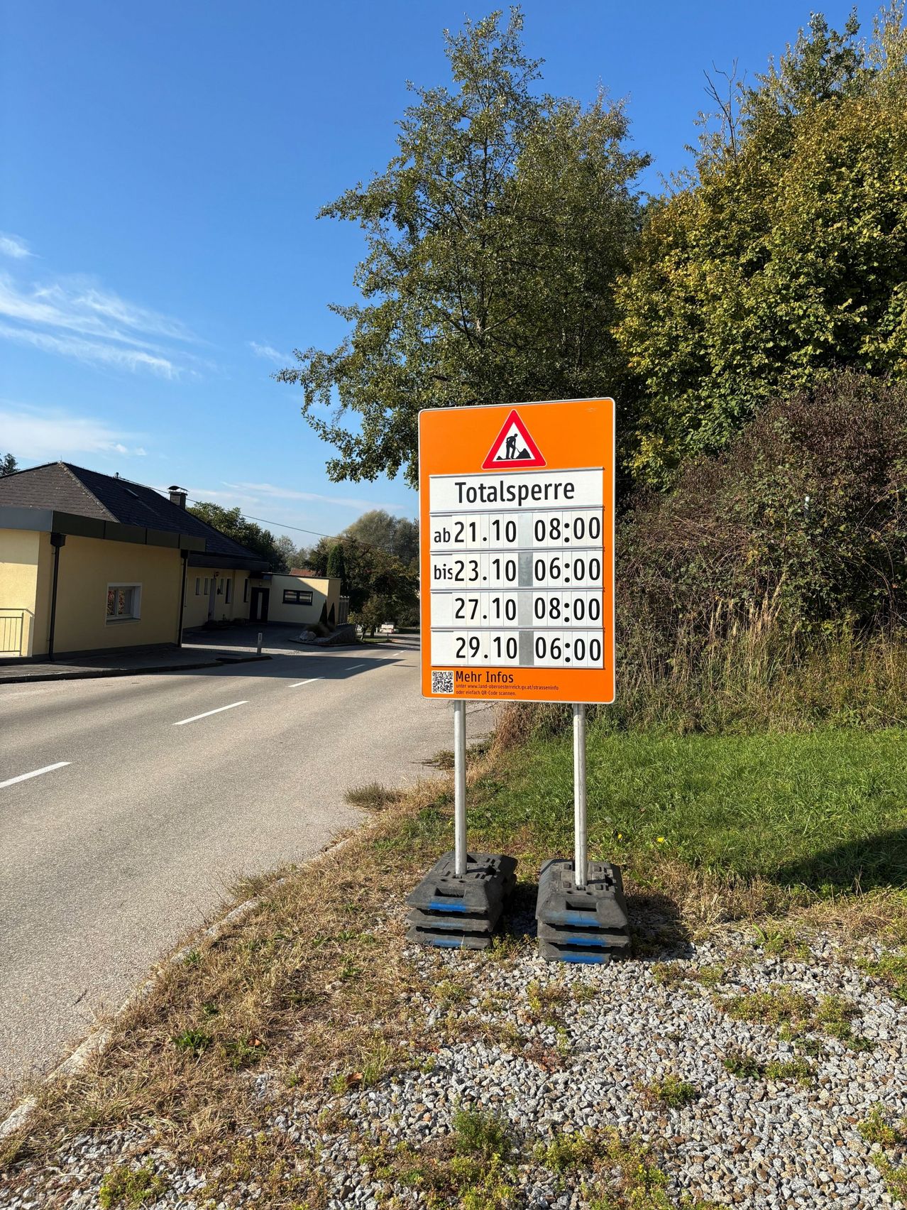 Ein orangefarbenes Schild mit einem Baustellensymbol und einem Zeitplan für Straßenarbeiten steht am Straßenrand.