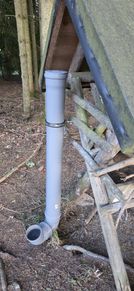 Eine Nahaufnahme eines grauen Metallpfahls, der mit einer Metallklemme an einer Holzstruktur in einem Waldgebiet befestigt ist.