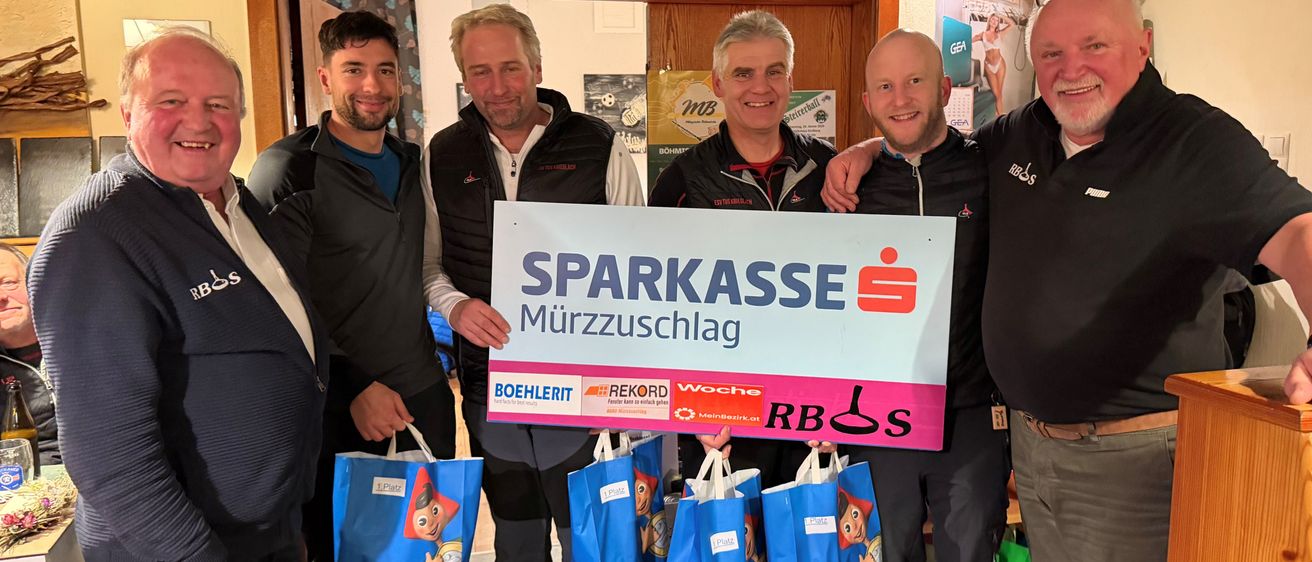 Sechs Männer halten Tüten und ein Schild mit den Worten 'SPARKASSE Murzzuschlag' vor einem Raum mit einer Tür und einem montierten Fernseher.