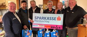 Sechs Männer halten Tüten und ein Schild mit den Worten 'SPARKASSE Murzzuschlag' vor einem Raum mit einer Tür und einem montierten Fernseher.
