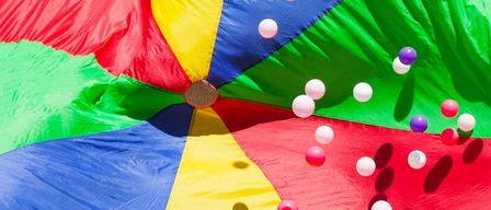 Ein farbenfroher Stoffbaldachin mit mehreren farbigen Luftballons darauf. Der Stoff ist auf dem Boden ausgebreitet und zeigt leuchtende rote, blaue, gelbe und grüne Farben.