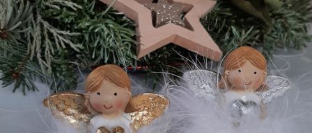 Zwei Engelsfiguren, eine mit goldenen Flügeln und eine mit silbernen Flügeln, sitzen unter einem Holzstern an einem Weihnachtsbaum.