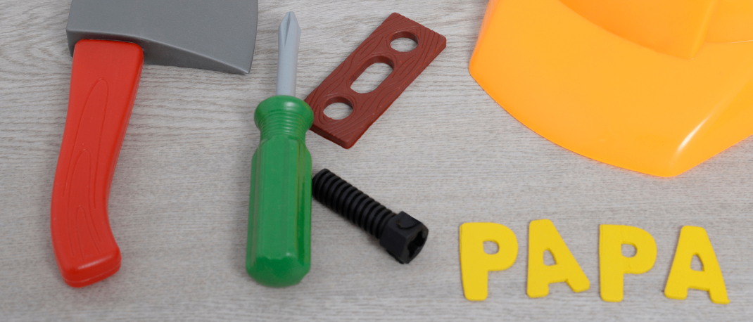 Eine Sammlung von Spielzeugwerkzeugen und einem Helm ist auf einer grauen Oberfläche mit dem Wort 'PAPA' angeordnet. Die Werkzeuge umfassen einen orangefarbenen Hammer, einen grünen Schraubendreher, ein rotes Holzobjekt und ein schwarzes Kunststoffteil. Ein gelber Kreis mit dem Wort 'EKIZ' ist links platziert.