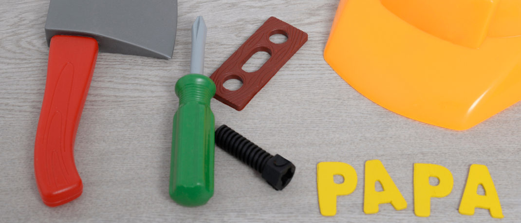 Ein Bausatz mit einem gelben Helm, einer roten Axt, einem grünen Schraubenzieher und einem Holzblock. Das Wort 'PAPA' besteht aus gelben Schaumstoffbuchstaben. Das EKIz-Logo befindet sich in der oberen linken Ecke.