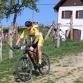 Ein Radfahrer in einem gelben Trikot und Helm fährt auf einem unbefestigten Weg mit der Nummer 35, in der Nähe von Barrieren und einem Haus mit einer braunen Tür.