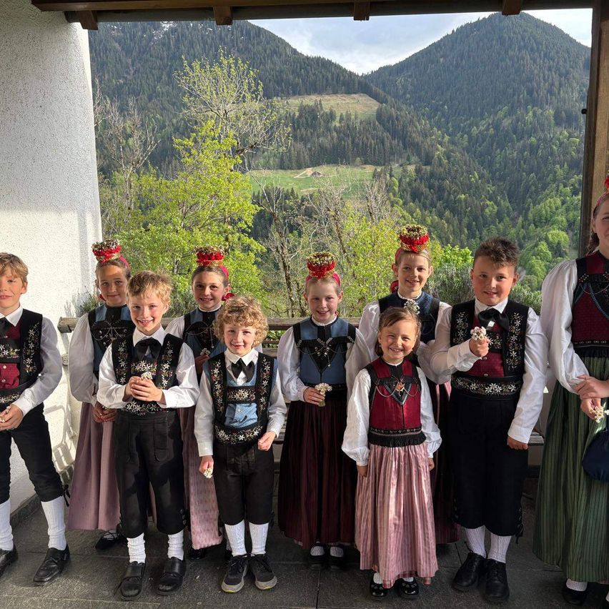 A group of children in traditional clothing pose for a photo with a mountainous landscape in the background.