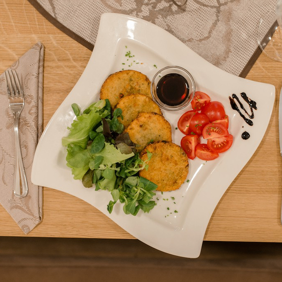 Ein Teller mit gebratenen Pasteten, Salat, Kirschtomaten und einer Schüssel Sauce auf einem Holztisch.