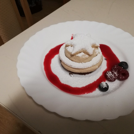 Ein Dessert auf einem weißen Teller mit einer sternförmigen Sahnehaube, umgeben von roter Sauce und garniert mit Blaubeeren und Himbeeren.