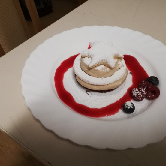 Ein Dessert auf einem weißen Teller mit einer sternförmigen Sahnehaube, umgeben von roter Sauce und garniert mit Blaubeeren und Himbeeren.