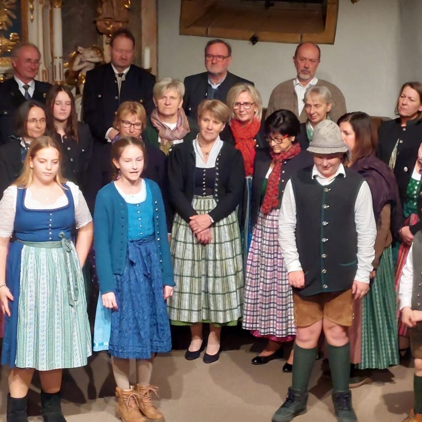 Eine Gruppe von Menschen in traditioneller Kleidung steht drinnen, lächelt und posiert für ein Foto. Der Hintergrund besteht aus einer Wand mit einem Spiegel und einem goldenen Design.