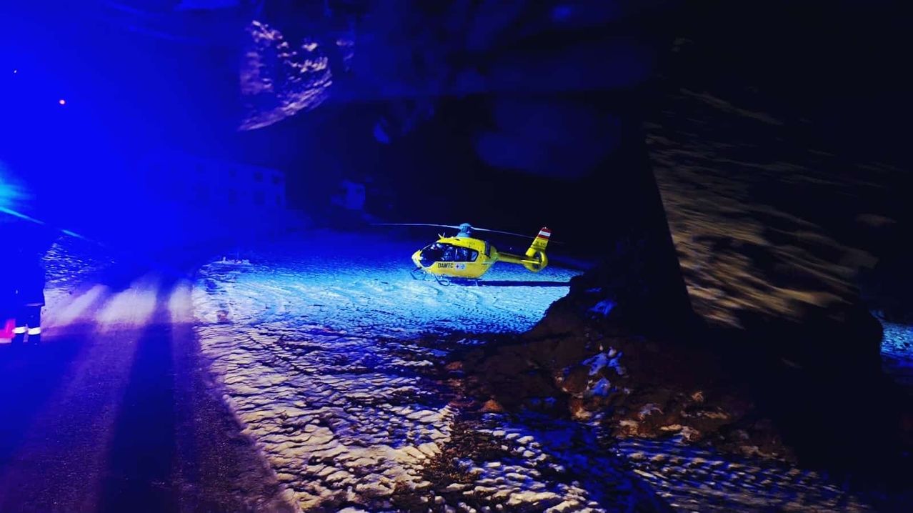 A yellow helicopter is parked in a cave, illuminated by blue lights. The helicopter is likely used for emergency rescue operations.