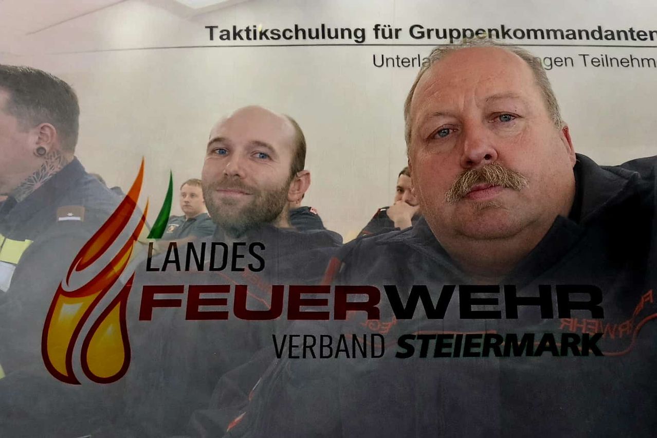 Zwei Feuerwehrleute stehen vor einem Schild, das Landesfeuerwehrverband Steiermark sagt.