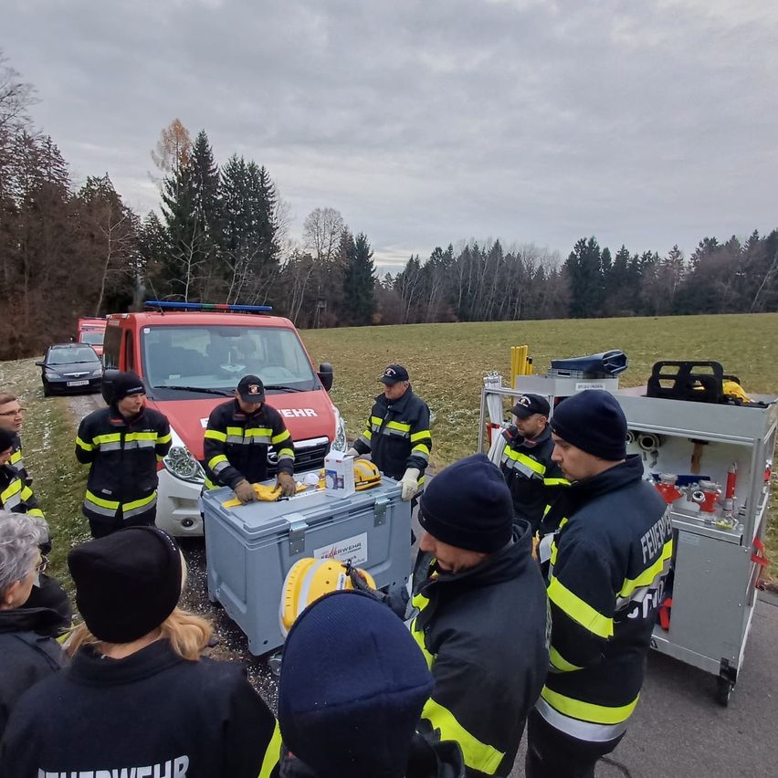 Feuerwehrleute versammeln sich um ein Fahrzeug, wahrscheinlich für eine Besprechung, mit Ausrüstung und einem Feld im Hintergrund.