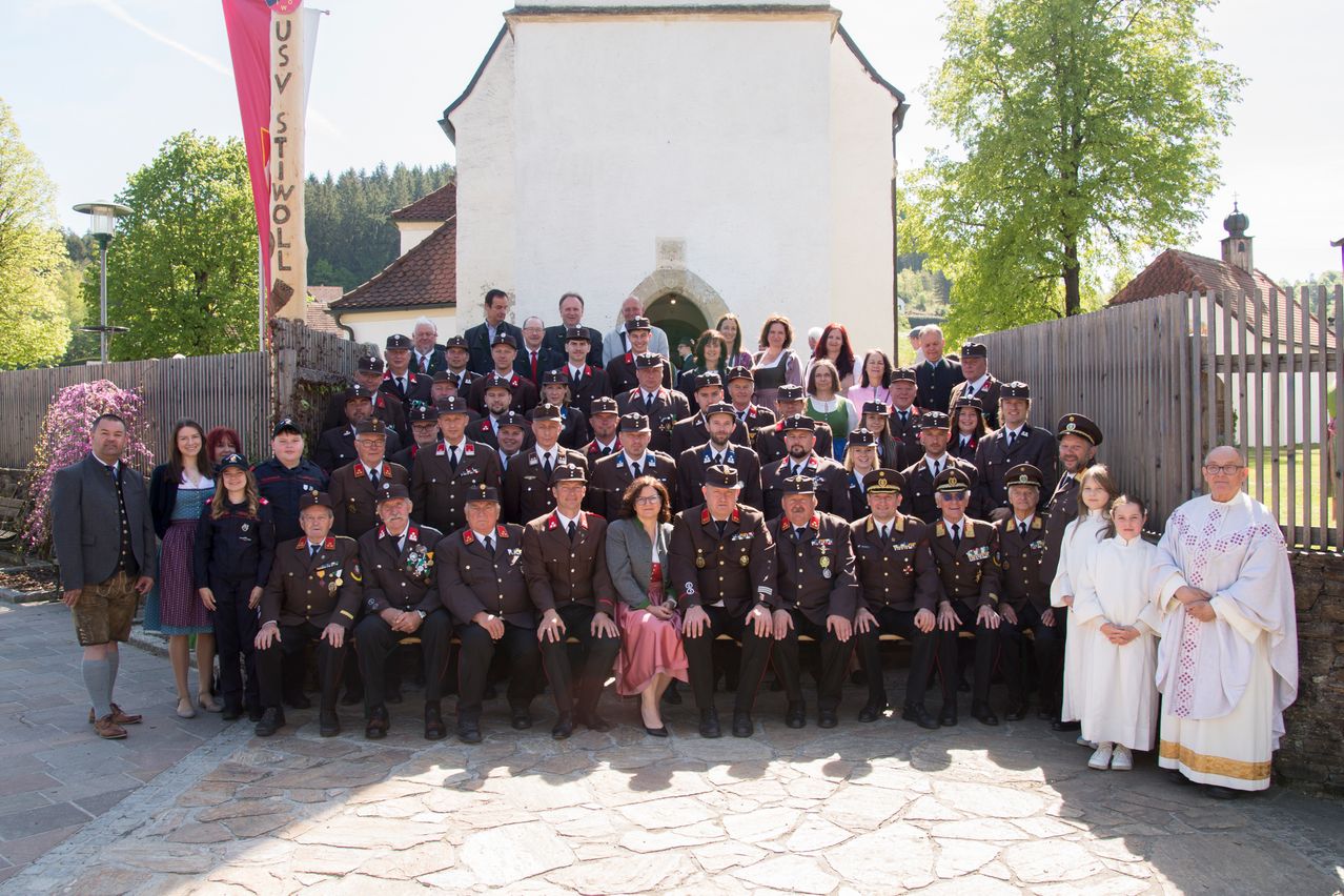 Eine große Gruppe uniformierter Personen, einschließlich Männer und Frauen, posiert für ein Foto vor einem historischen Gebäude. Einige sitzen, andere stehen.