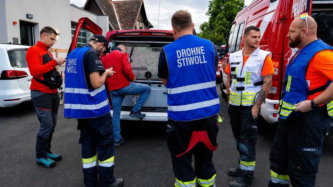 Vier Notfallhelfer in reflektierenden Westen stehen um ein Fahrzeug. Ein Mann sitzt hinten, während ein anderer Mann neben ihm steht.