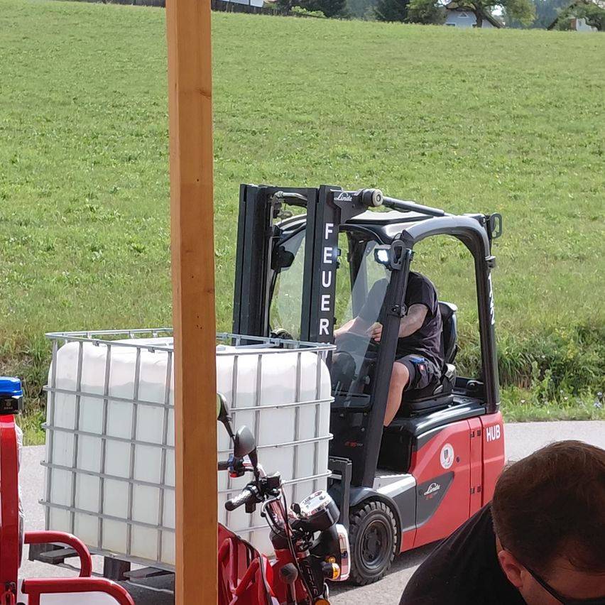 Ein Gabelstapler mit einem großen weißen Tank ist auf einem Feld geparkt. Ein Mann sitzt auf dem Fahrersitz.