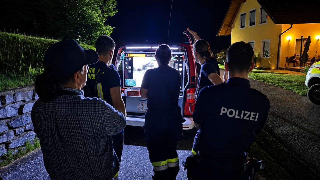 Rettungskräfte versammeln sich nachts um ein Fahrzeug, auf dem Bildschirm ist ein Bild zu sehen. Ein Polizeibeamter steht rechts.