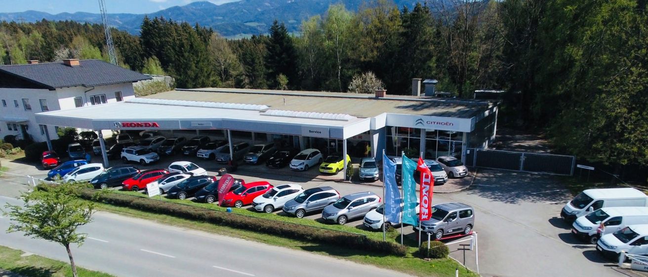 Ein Luftbild einer Citroen-Vertretung mit mehreren geparkten Autos, darunter ein roter Honda und ein gelber Citroen.