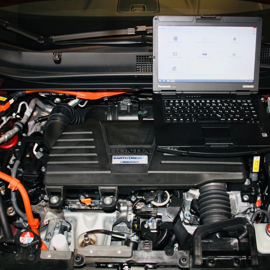 Ein Laptop liegt auf einem Honda Earth Dreams Motor und zeigt die Motorkomponenten und den Bildschirm des Laptops, der eine Software-Oberfläche anzeigt.