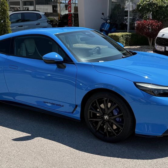Ein blauer Sportwagen mit schlankem Design ist vor einem Gebäude mit einem Roller und einem weißen Auto geparkt.