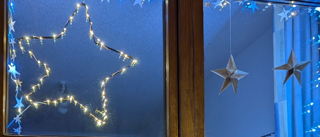 Ein Fensterdisplay mit einem Stern aus Lichtern, einem Schneemann und Weihnachtshäusern mit einem Weihnachtsbaum in der Mitte, alles für Weihnachten dekoriert.