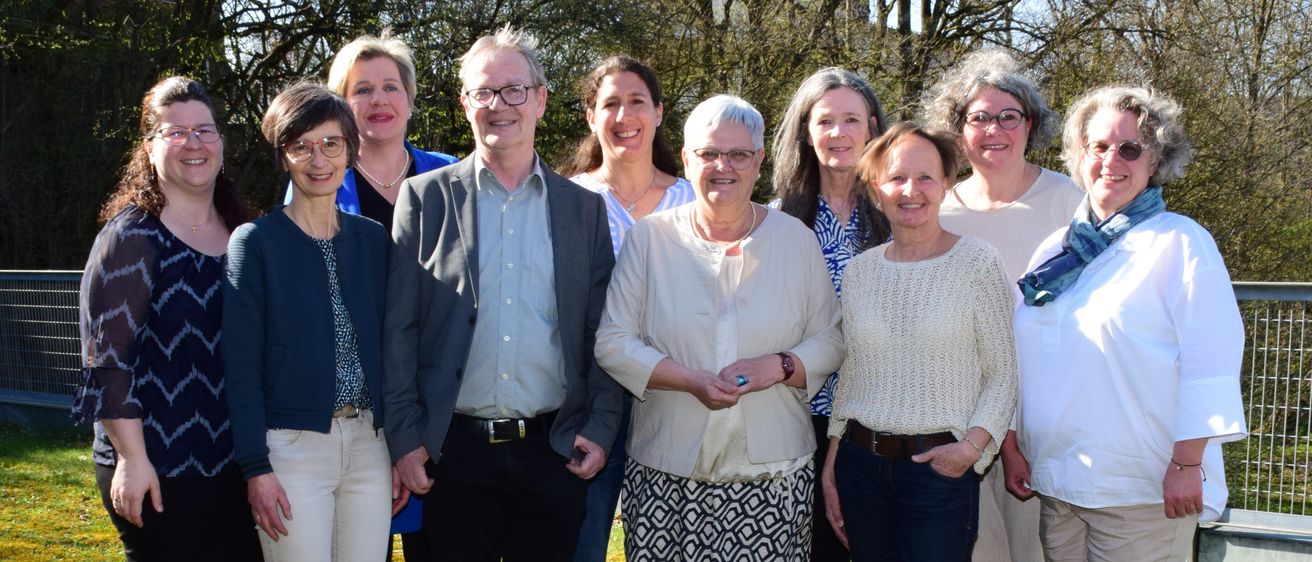 Eine Gruppe lächelnder Erwachsener posiert für ein Foto auf einer Rasenfläche mit Bäumen im Hintergrund.
