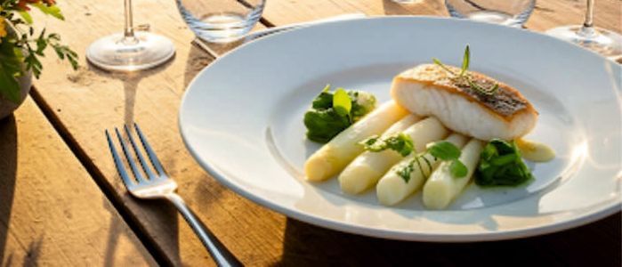 Ein Teller mit Essen und Weingläsern auf einem Tisch mit einem Weinberg im Hintergrund und dem Text Wein und Essen über dem Teller geschrieben
