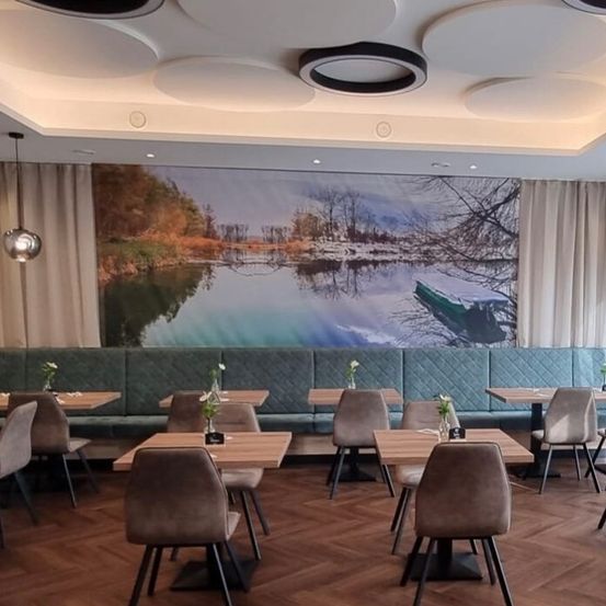 Ein Restaurant-Innenraum mit Holzboden, weißer Decke, einer großen Wandmalerei und mehreren leeren Tischen mit Stühlen und Blumen.