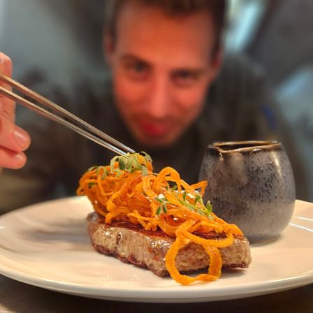 Ein Mann isst ein Gericht mit Steak, das mit Karottenstreifen und Kräutern belegt ist.