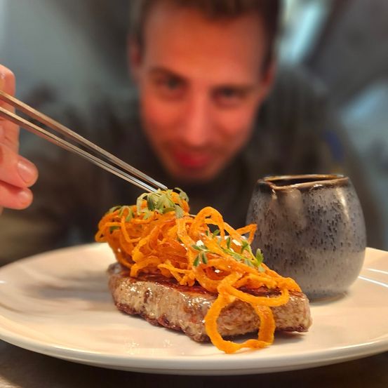 Ein Mann isst ein Gericht mit Steak, das mit Karottenstreifen und Kräutern belegt ist.