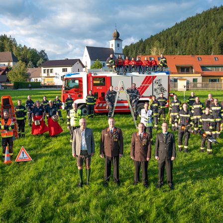 Eine Gruppe von Feuerwehrleuten steht vor einem Feuerwehrauto, auf dem einige sitzen, in Uniform gekleidet und posiert für ein Foto auf einem Feld mit einem Berg im Hintergrund.